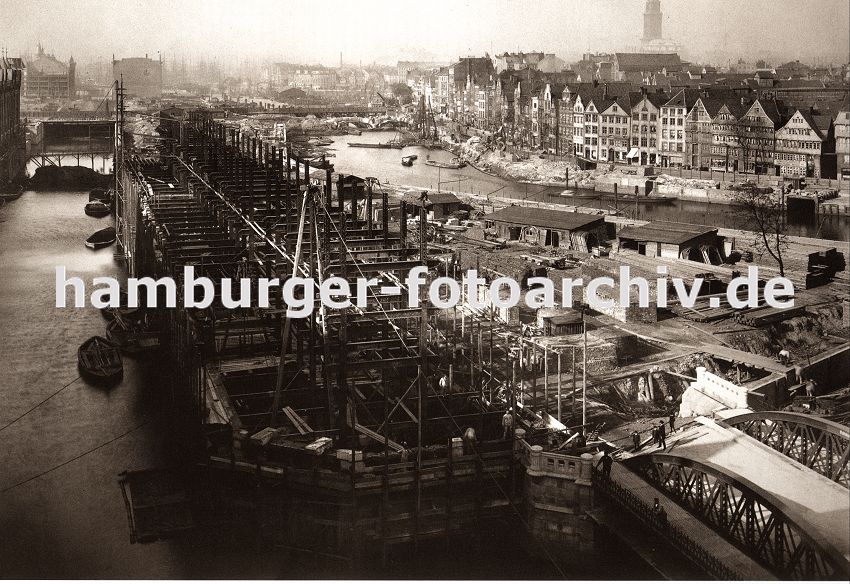 01147714 Architekturfotos von Hamburg - der Bau der neuen Hamburger Speicherstadt hat begonnen - die Fleete sind ausgehoben und werden mit neu errichteten Brcken berspannt, Schuten transportieren das Baumaterial. Im Vordergrund wird der Speicherblock G gebaut - die Eisentrger ragen aus der Baustelle. Am neu entstehenden Zollkanal, der die Zollgrenze des Hamburger Freihafens bildet werden neue Kaimauern hochgezogen - ganz im Hintergrund ist ein Ausschnitt vom Hamburger Michel zu erkennen.