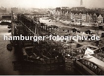 01147714 der Bau der neuen Hamburger Speicherstadt hat begonnen - die Fleete sind ausgehoben und werden mit neu errichteten Brcken berspannt, Schuten transportieren das Baumaterial. Im Vordergrund wird der Speicherblock G gebaut - die Eisentrger ragen aus der Baustelle. Am neu entstehenden Zollkanal, der die Zollgrenze des Hamburger Freihafens bildet werden neue Kaimauern hochgezogen - ganz im Hintergrund ist ein Ausschnitt vom Hamburger Michel zu erkennen.