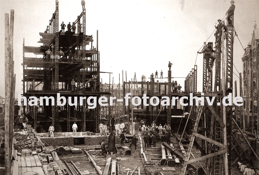 01147715 Hamburg Fotografie Architekturgeschichte : :  die Eisentrger des Speicherblock H werden hoch gezogen - Bauarbeiter balancieren auf dem Gerst; einfach zusammen genagelte Holzleitern werden zum Besteigen der Hamburger Grossbaustelle benutzt. Auf provisorisch verlegten Gleisen kann Baumaterial per Handwagen ber das Gelnde der entstehenden Speicherstadt transportiert werden. 