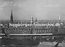 01147721 Blick ber den Sandtorhafen und dem Sandtorkai zur Hamburger Speicherstadt mit ihren Giebeln und Trmen der Backsteinarchitektur. Schiffe liegen am Kai und werden entladen und die Ladung in den Lagerschuppen am Kaispeicher verstaut. Hinter den Speichern das Panorama Hamburgs mit seinen markanten Trmen: links die Nikolaikirche, dann folgt der Turm der Hauptkirche St. Katharinen, deren Kirchspiel auch fr die Speicherstadt zustndig ist. Rechts daneben der Rathausturm und am rechten Rand der Turm der Hamburger St. Petrikirche. 