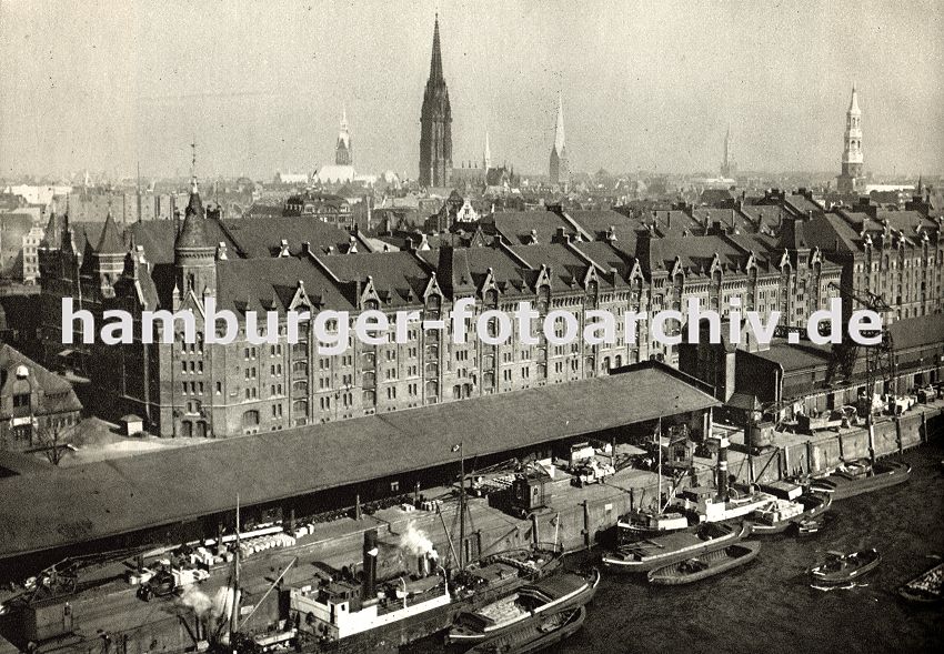 01147723 Blick auf den Sandtorkai und seine langen Lagerschuppen - bewegliche Hafenkrane fahren auf Schienen und entladen die Schiffe, die am Kai liegen. Die Ware wird in den Schuppen gelagert oder direkt auf Binnenschiffe oder Khne verladen, die sie weiter transportieren. Im Hintergrund das historische Hamburger Panorama mit den Kirchtrmen der Hansestadt.