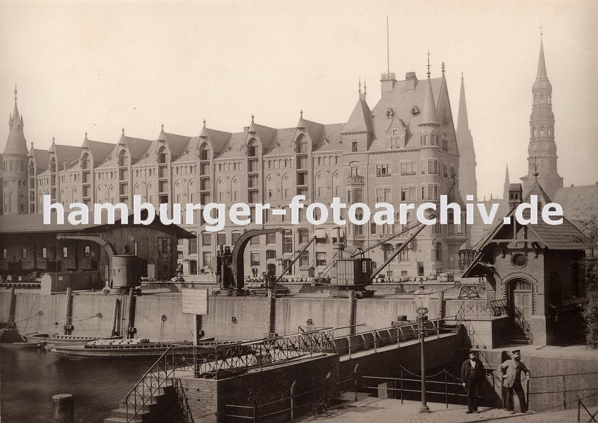 01147726 im Vordergrund die Schleuse, die den Sandtorhafen und Brooktorhafen trennt - ein Kahn liegt an der Kaimauer, er ist an den eingelassenen Metallringen vertut. Seine Ladung besteht aus Holzfssern - vor dem Speichergebude am Sandtorkai liegt eine grosse Anzahl dieser Fsser und warten auf den Abtransport. Drei unterschiedliche Krne, die auf Schienen bewegt werden, stehen am Kai. Hinter dem Schleuserhuschen die Kirchtrme der St. Katharinenkirche und der Nicolaikirche, zwei der fnf Hamburger Hauptkirchen.