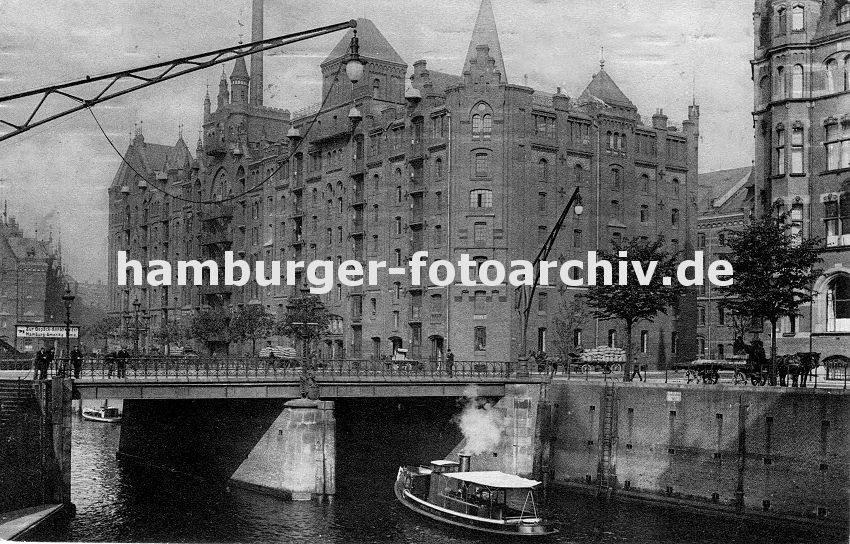 01147728 Blick ber die St. Annenbrcke zum Speicherblock R - Wagen sind mit Stapeln von Scken beladen und werden von Pferden gezogen - re. sitzt ein Kutscher auf dem Bock seines leeren Wagens und wartet auf Ladung. Eine Dampfbarkasse fhrt unter die Brcke, Mnner stehen am Eisengelnder und sehen auf das Fleet. Hinter ihnen weist ein grosses Schild mit Hand und ausgestreckten Zeigefinger auf die Gepck Annahme der Hamburg Amerika Linie hin. 