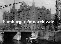 01147728 Blick über die St. Annenbrücke zum Speicherblock R - Wagen sind mit Stapeln von Säcken beladen und werden von Pferden gezogen - re. sitzt ein Kutscher auf dem Bock seines leeren Wagens und wartet auf Ladung. Eine Dampfbarkasse fährt unter die Brücke, Männer stehen am Eisengeländer und sehen auf das Fleet. Hinter ihnen weist ein grosses Schild mit Hand und ausgestreckten Zeigefinger auf die Gepäck Annahme der Hamburg Amerika Linie hin. 