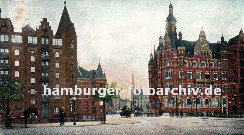 01147732 Hamburger Bilder - Hamburg Fotos -  Blick ber die St. Annenbrcke zur Kornhausbrcke - im Hintergrund ist der Kirchturm der St. Petrikirche zu erkennen. Links steht ein Pferd mit Decke in seiner Deichsel, zwei kleine Strassenbume sind an den Strassenrand gepflanzt - drei hochbeladene Karren von Pferden gezogen berqueren die St. Annen Brcke; rechts der Block U, das sogenannte Speicherstadt Rathaus, in dem die Verwaltung ihren Sitz hat und links der Speicherblock  R, dahinter der Block P.