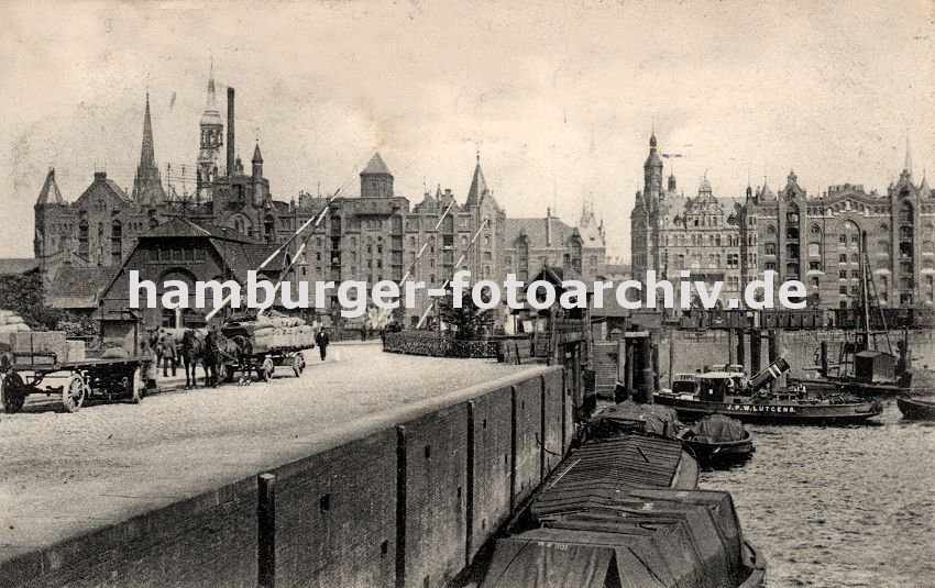 01147733 historisches Hamburg : Fotos -  Khne mit Ladung, die mit Planen abgedeckt ist, liegen am Kai vom Brooktorhafen; ein Schlepper hat seinen Schornstein umgelegt, damit er unter der Brcke Richtung Sandtorhafen fahren kann. An der Zollstation sind die Schlagbume oben - Pferdewagen mit Ladung stehen am Kai. Vor den Speichergebuden stehen rechts im Vordergrund Eisenbahnwaggons am Brooktorkai. 