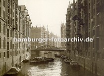 01147736 Schuten im Fleet in der Hamburger Speicherstadt - die Khne sind mit Scken beladen und an den Ringen, die in der Speichermauern eingelassen sind fest gemacht. Eine ber dem Wasser hngende Lampe soll die Arbeiten in der Dunkelheit erleichtern. Neben dem eisernen Rundbogen der Brcke ber den Fleet steht links eine Litfasule. 