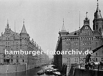 01147741 Blick auf die Speicherblocks A und J  an der Kehrwiederspitze; rechts ein stationrer Kran, dahinter sind Handkarren und Pferdewagen abgestellt, die fr den Transport von Waren innerhalb der Speicherstadt verwendet werden. Oben am Giebel ist des rechten Speichers unter dem Eisendekor eines Segelschiffes eine grosse Uhr angebracht. Auf dem Kehrwiederfleet liegt eine Kastenschute, ein Kahn hat lngsseits festgemacht und lscht seine Ladung mit Scken.