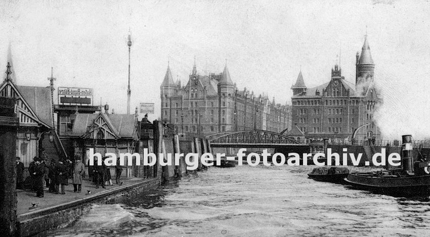 01147742 hamburgfotos - Anleger am Baumwall; auf dem Ponton stehen Passagieren und warten auf das Schiff - ein Schild macht Werbung fr die Hafenrundfahrt. Ein Schlepper zieht eine beladene Schute vom Hamburger Freihafen Richtung Elbe. Im Hintergrund die beiden Speicherblcke A und J, die am Kehrwiederfleet liegen.