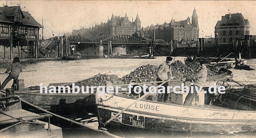 01147743 Hamburgbilder -  Blick vom Bauwall Richtung Niederbaumbrcke - Schiffer legen mit ihren Schuten an; mit langen Bootshaken ziehen sie ihre  Boote lngsseits - einer der Khne ist hoch mit Kohlen beladen. nRechts das Gebude der Freihafen-Polizeiwache, dahinter erstrecken sich die Speicher der Hamburger Speicherstadt.