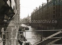 507_061_15 Blick von der Kehrwiederstegbrcke auf das Brooksfleet; Schuten und Barkassen liegen an der Gebudemauer des Speichergebudes Block D. Die Kaffeeladung eines der Khne wird gerade gelscht. Eine Hieve Scke wird mit der Winde, die sich unter dem Dach des Speichers befindet auf den Lagerboden gebracht. Auf der rechten Fleetseite die neogotischen Backsteinfassaden der Speicherblcke L, M, N und O - im Hintergrund die Kibbelstegbrcke.