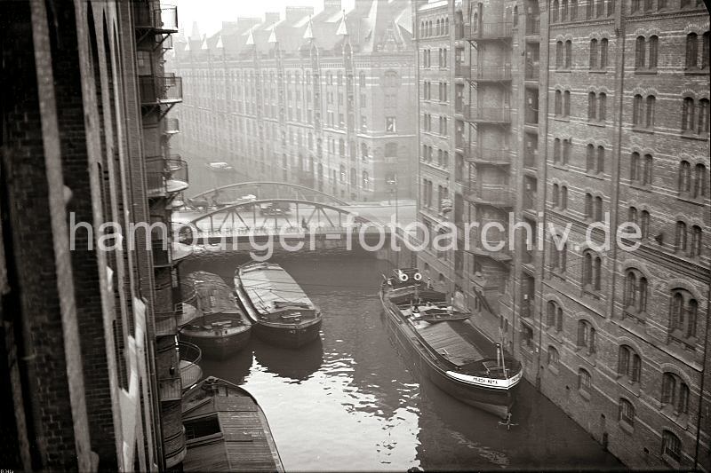 Alte Bilder Speicherstadt Hamburg aus dem Bildarchiv der HHLA. Brooksfleet - Kibbelstegbrcke, Binnenschiff und Schuten an den Speichern. 507_08_B_341a Blick vom Speichergebude Q auf das Brooksfleet; abgedeckte Schuten liegen an der Mauer des Speichers - auf der gegenberliegendem Speicher G wird ein Binnenschiff be- oder entladen, eine Hieve Scke hngt ber dem Schiff an der Winde. Auf der Kibbelstegbrcke fhrt ein Pferdefuhwerk; dahinter die Speicher F + E.