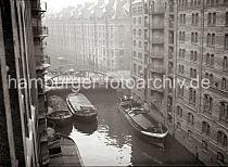 507_08_B_341a Blick vom Speichergebude Q auf das Brooksfleet; abgedeckte Schuten liegen an der Mauer des Speichers - auf der gegenberliegendem Speicher G wird ein Binnenschiff be- oder entladen, eine Hieve Scke hngt ber dem Schiff an der Winde. Auf der Kibbelstegbrcke fhrt ein Pferdefuhrwerk; dahinter die Speicher F + E.