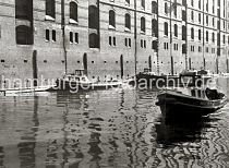 507_09_2 Barkassen liegen an der Mauer eines Backstein-Speichers in der Speicherstadt; die Mauern der  Speicherge- bude sind mit Holzstmmen gegen Beschdigungen durch Schiffe geschtzt. Aus einigen Luken hngen Strickleitern - ber dieses Fallreep kann das Schiff vom Lager aus bestiegen werden.