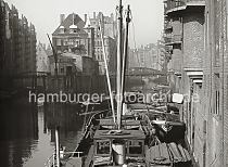 507_11_5 Blick von der Poggenmhlenbrcke auf die Fleete der Hamburger Speicherstadt. Links liegt das Hollndische Brooks Fleet mit den Speichern x und V sowie rechts das Wandrahmsfleet mit dem Speichergebude W und hinter der Brcke Dienerreihe die Speicher T und S. Ein Frachter hat am Speicher W fest gemacht, an der Winde wird ein Ballen transportiert. Dahinter eine Schute, an deren Bug die Bezeichnung "Allied Forces" steht.