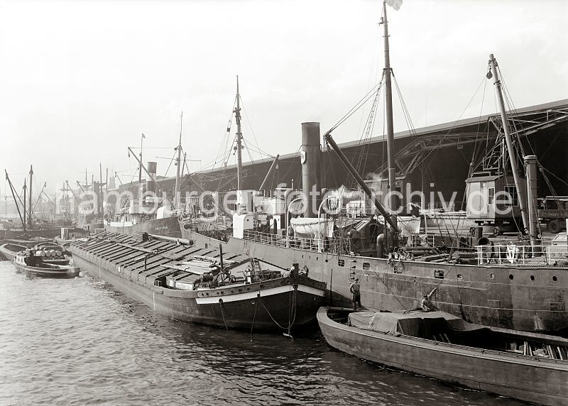 Hamburger Hafenfotografien aus dem Bildarchiv der Hamburger Hafen und Logistik AG HHLA. Gterumschlag am Dalmannkai des Hamburger Grasbrookhafens.  603_14_680 Arbeit im Hamburger Hafen - die Ladung der Schiffe wird gelscht und neue Fracht mit den Hafenkranen und schiffseigenen Ladebumen an Bord gebracht. Die Gter kommen von der Landseite aus den Kaischuppen des Dalmankais oder von Schuten und Binnenschiffen die an der Wasserseite der Motorschiffe liegen. Im Hintergrund ist zwischen dem Gewirr der Schiffsmasten und Schiffsschornsteine der Turm des Kaispeischers A zu erkennen.