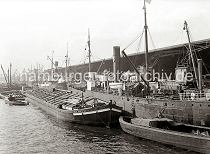 603_14_680 Arbeit im Hamburger Hafen - die Ladung der Schiffe wird gelscht und neue Fracht wird mit den Hafenkranen und schiffseigenen Ladebumen an Bord gebracht. Die Gter kommen von der Landseite aus den Kaischuppen des Dalmankais oder von Schuten und Binnenschiffen, die an der Wasserseite der Motorschiffe liegen. Im Hintergrund ist zwischen dem Gewirr der Schiffsmasten und Schiffsschornsteinen der Turm des Kaispeischers A zu erkennen.